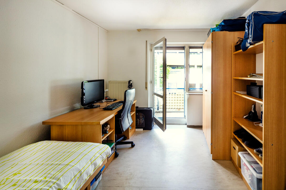 Zimmer mit Bett, Schreibtisch, Schrank und großem Fenster im Straußäcker 2