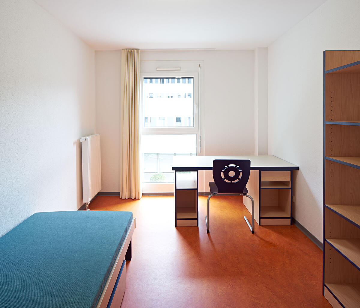 Zimmer mit Bett, Schreibtisch und Regal im Wohnheim in der Fabrikstraße