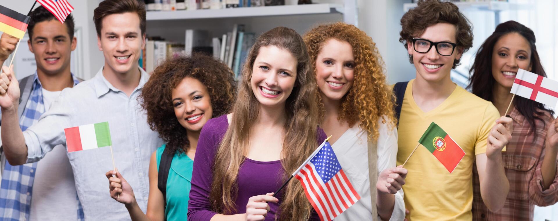 Internationale Studierende stehen in einer Reihe nebeneinander und halten Flaggen aus verschiedenen Ländern in der Hand