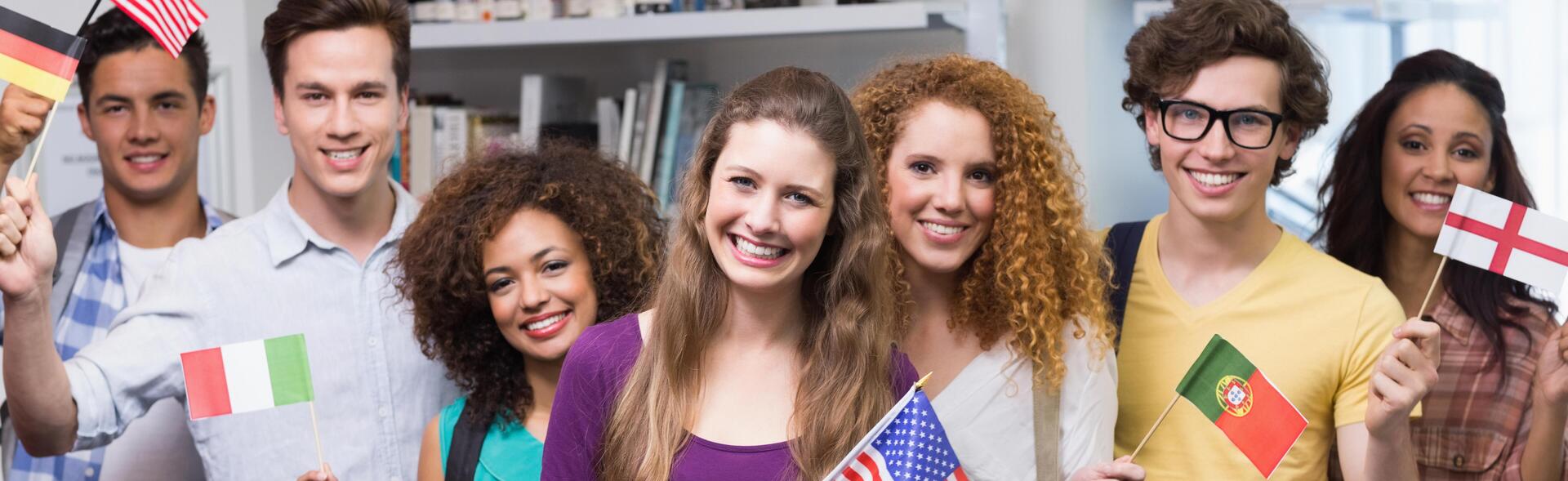 Internationale Studierende stehen in einer Reihe nebeneinander und halten Flaggen aus verschiedenen Ländern in der Hand