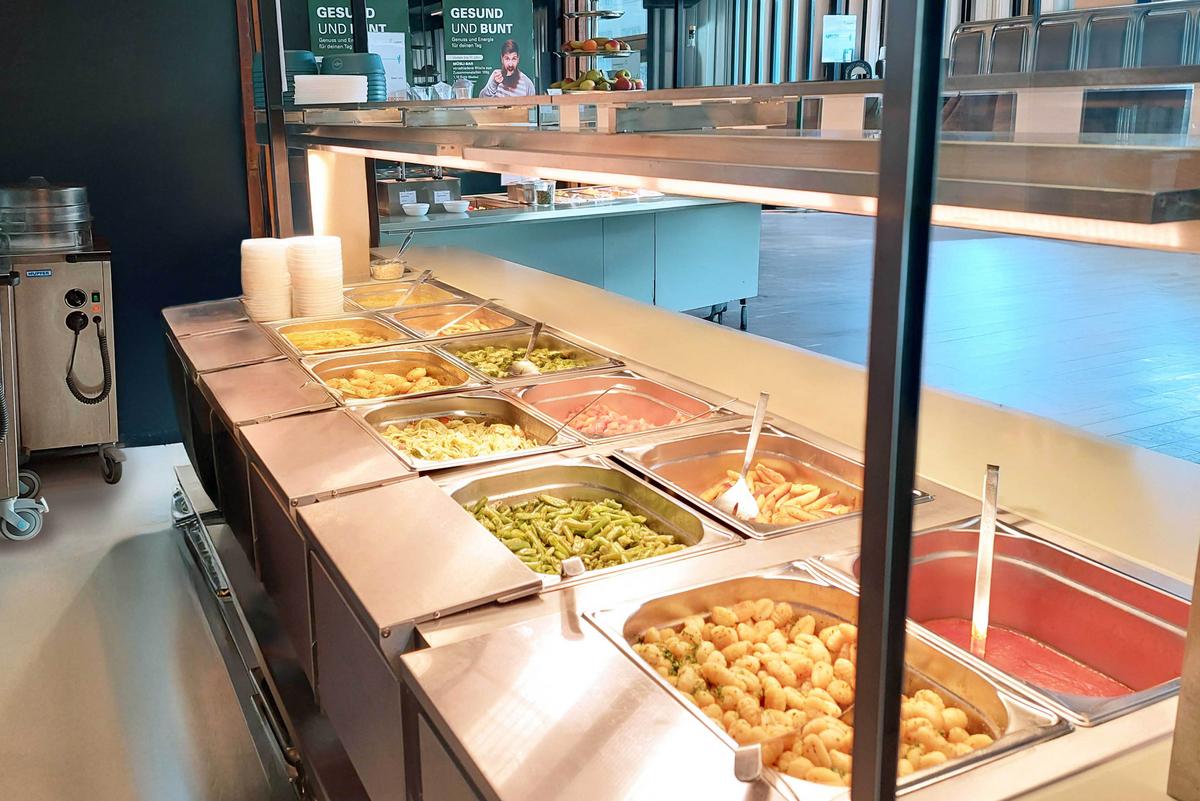 Warmes Buffet in der Mensa ABK mit verschiedenen Essen: Kartoffelspalten, Bohnen, Gnocchi, Nudeln, Brokkoli, Pommes und Soße