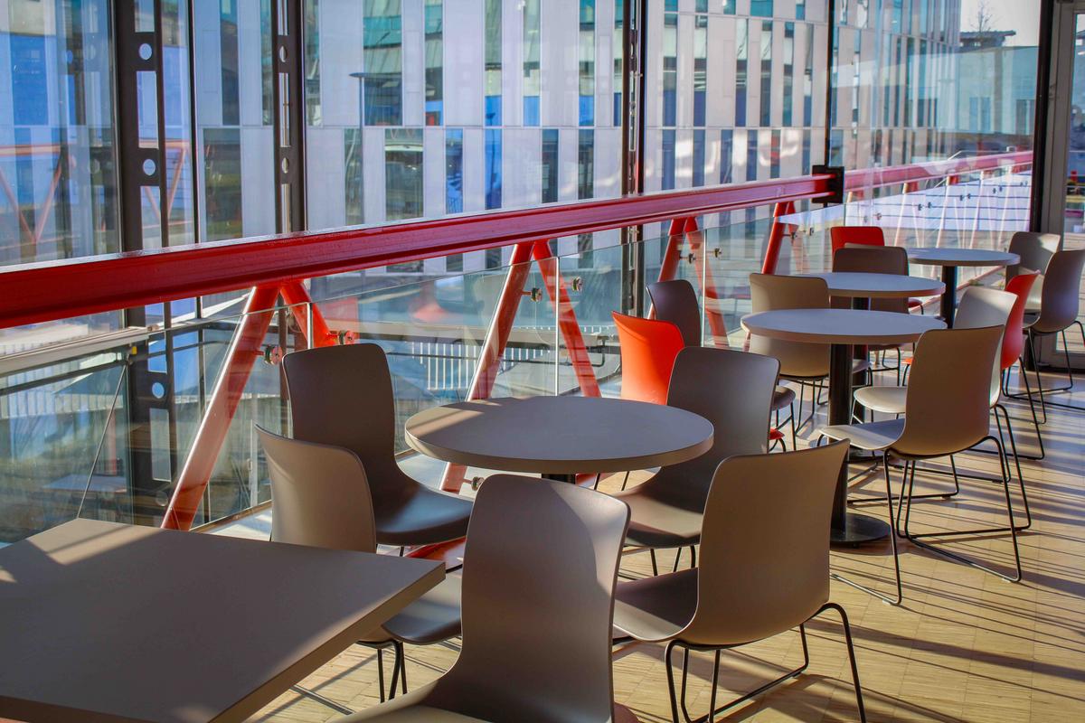 Graue und Orangene Stühle stehen um runde graue Tische