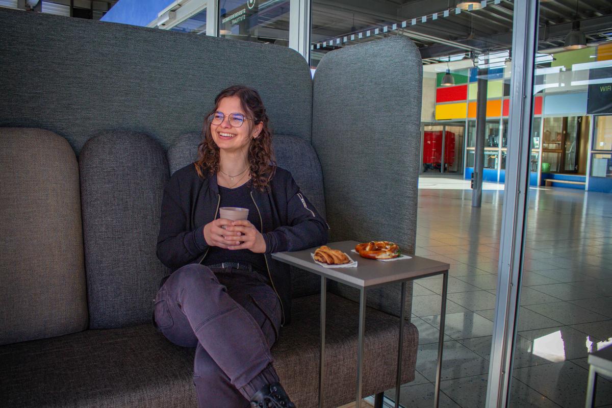 Frau sitzt mit einem Kaffee und Backwaren in einem grauen Sessel