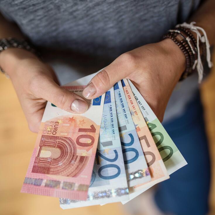 Person hält einen 10, 20, 50 und 100 Euro-Schein aufgefächert in der Hand
