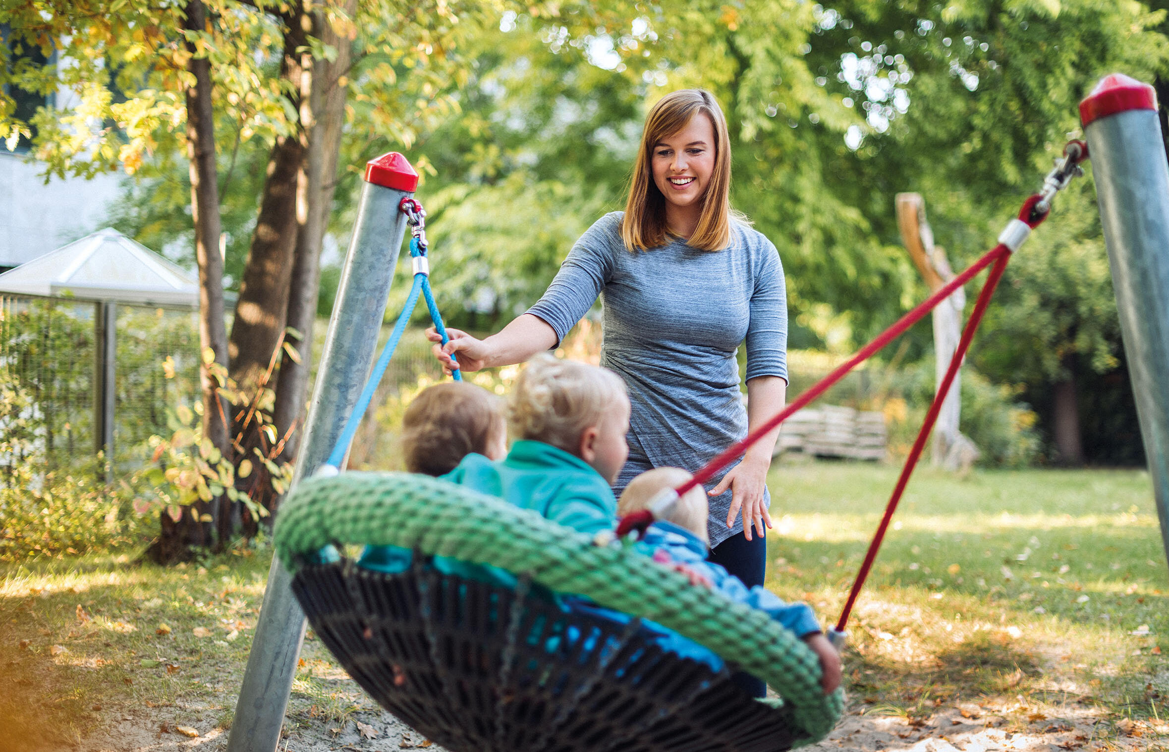 Erzieherin schaukelt drei Kleinkinder in einer Nestschaukel