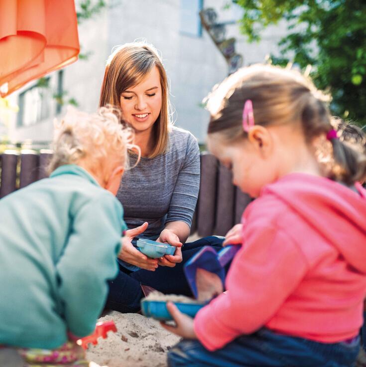 Erziehrin spielt mit Kindern im Sandkasten