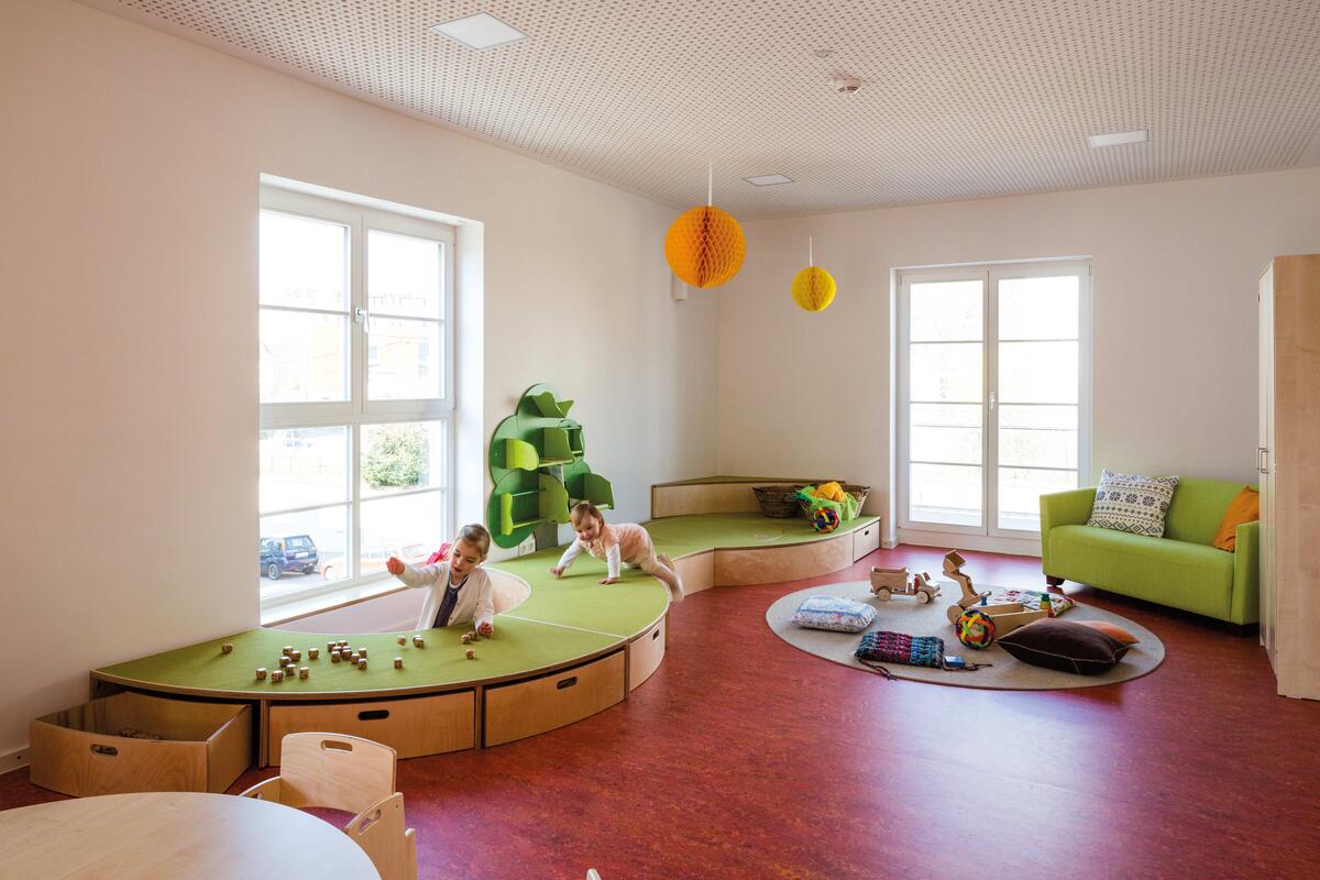 Group room of the Villa MiO day care centre with green furniture, in which two toddlers play