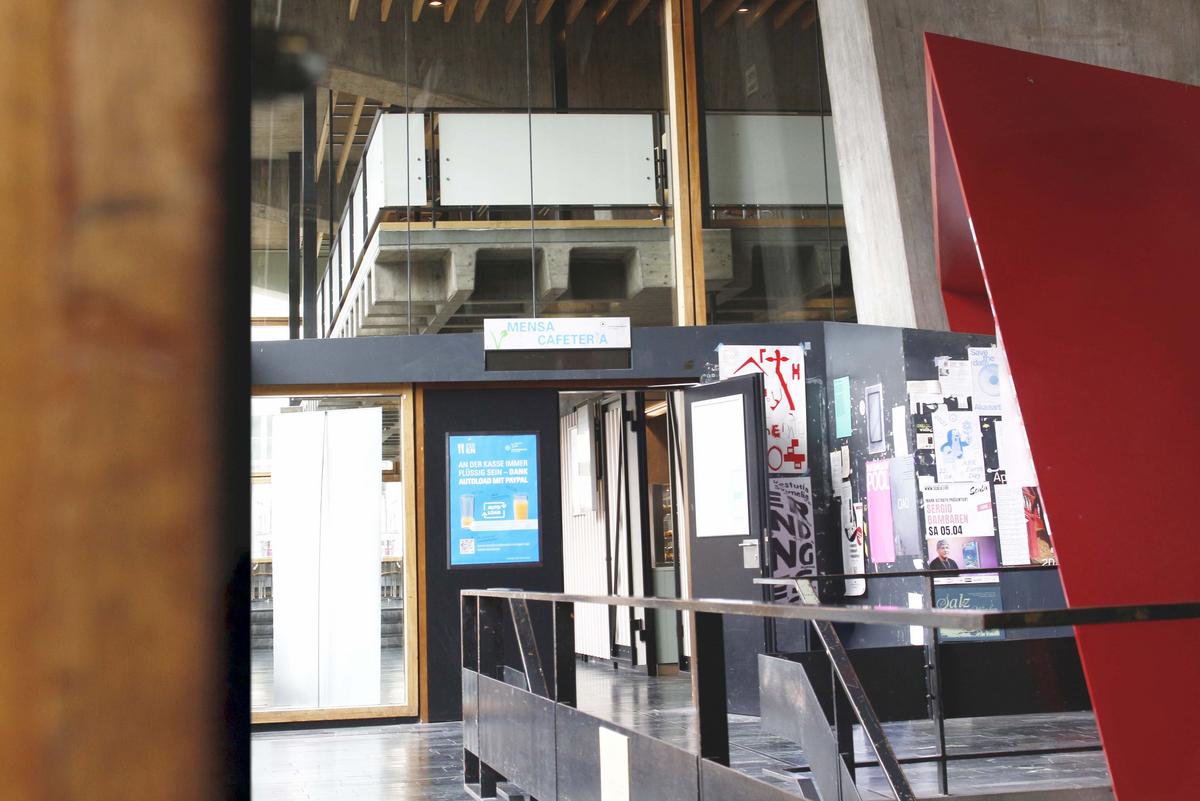 Eingangsbereich der Mensa Kunstakademie. Links neben dem Eingang hängt ein Bildschirm mit Informationen zu Autoload. Über der Türe hängt ein Schild "Mensa Cafeteria"