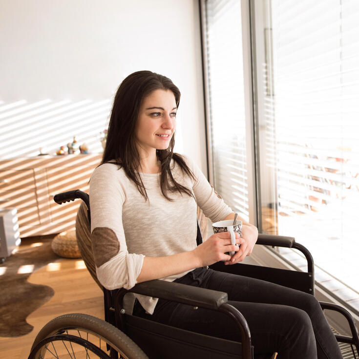 Female student in wheelchair watches the world outside the window 