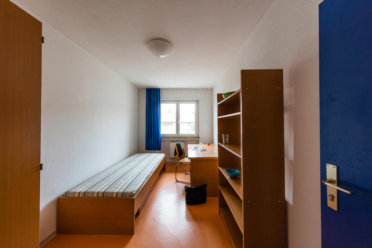 Zimmer mit Bett, Schreibtisch und Regal im Wohnheim in der Landhausstraße