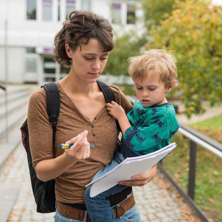 Eine Studentin hält ihr Kind auf dem Arm und füllt ein Formular aus