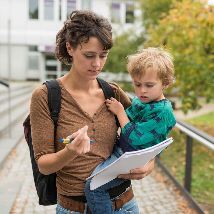 Eine Studentin hält ihr Kind auf dem Arm und füllt ein Formular aus