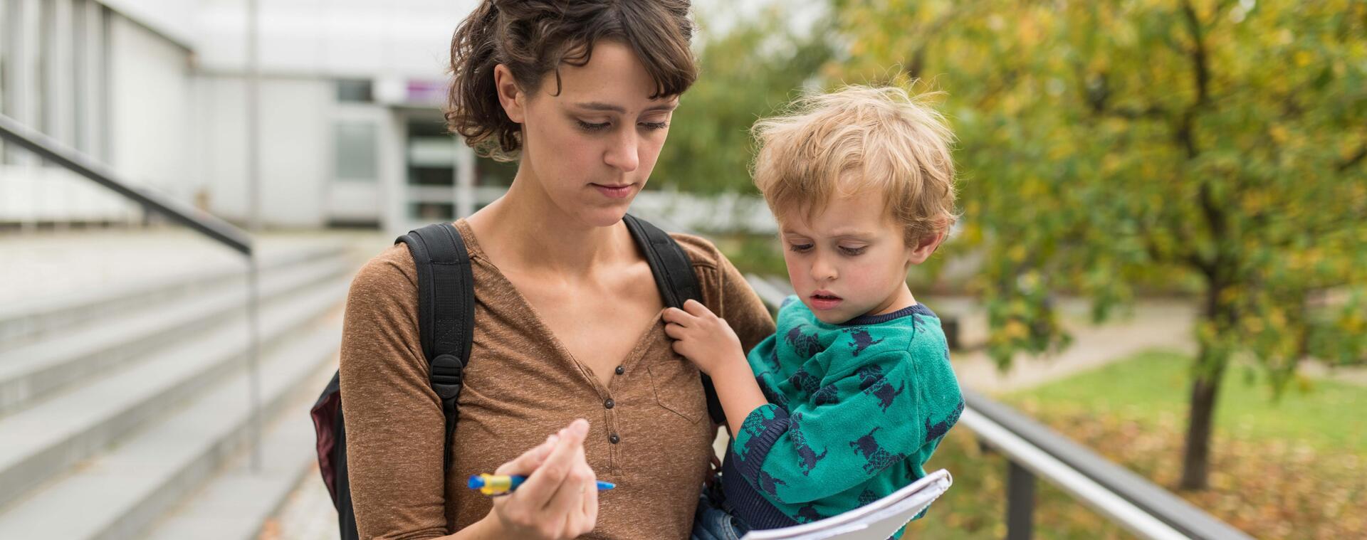 Eine Studentin hält ihr Kind auf dem Arm und füllt ein Formular aus