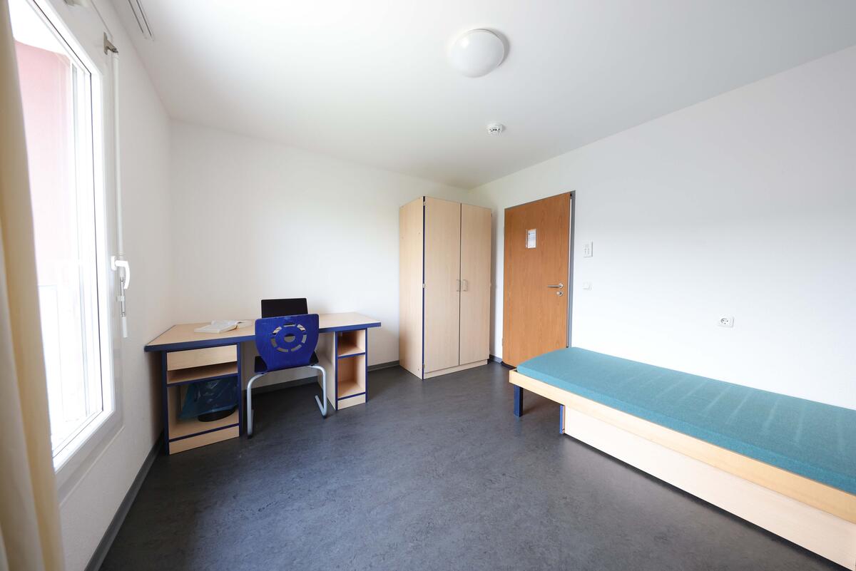 Zimmer mit Bett, Schreibtisch und Schrank im Wohnheim in der Fabrikstraße