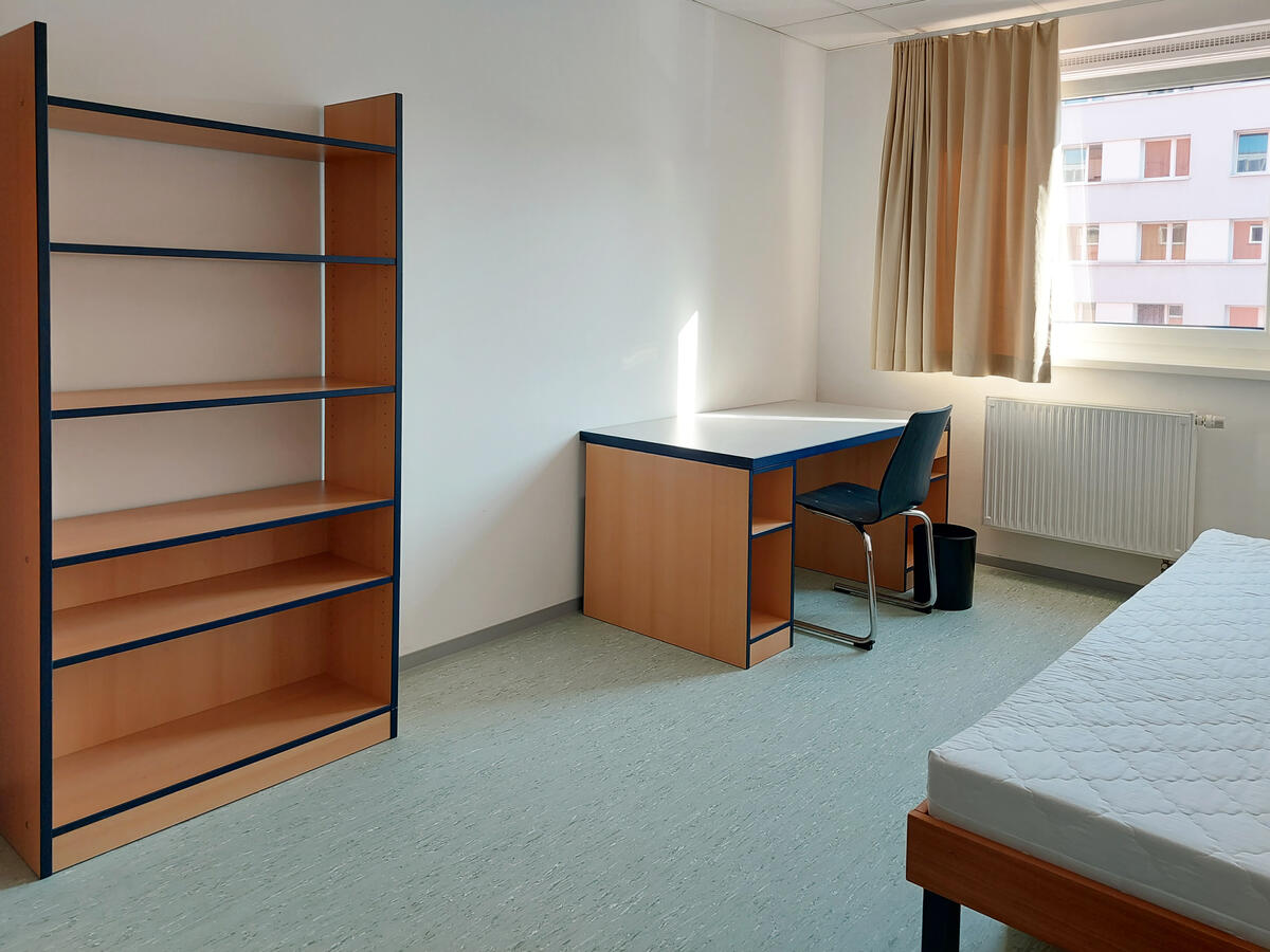 Zimmer in der Heilmannstraße mit Regal, Schreibtisch, Stuhl und Bett