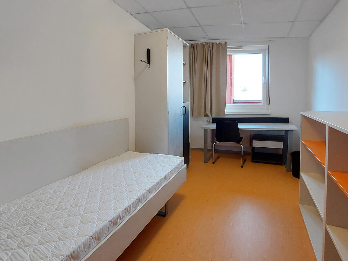 Zimmer in der Heilmannstraße mit Bett, Schrank, Schreibtisch, Stuhl und Regalen