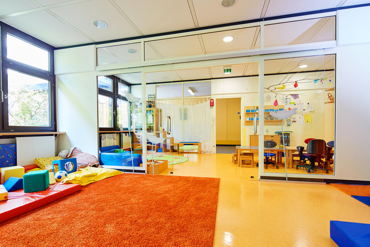 Group room with large play corner with carpet, various seating and toys in the daycare center Löwenzahn