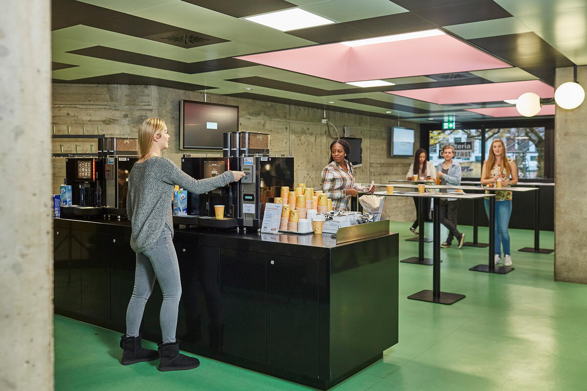 Photo of the coffee machine and students standing at bar tables in the background