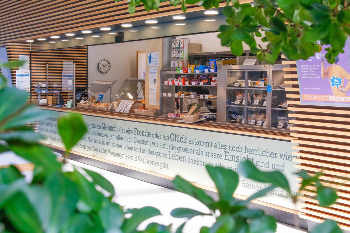 Theke der Cafeteria Göppingen mit süßen und salzigen Snacks in der Auslage.  Im Vordergrund stehen Pflanzen