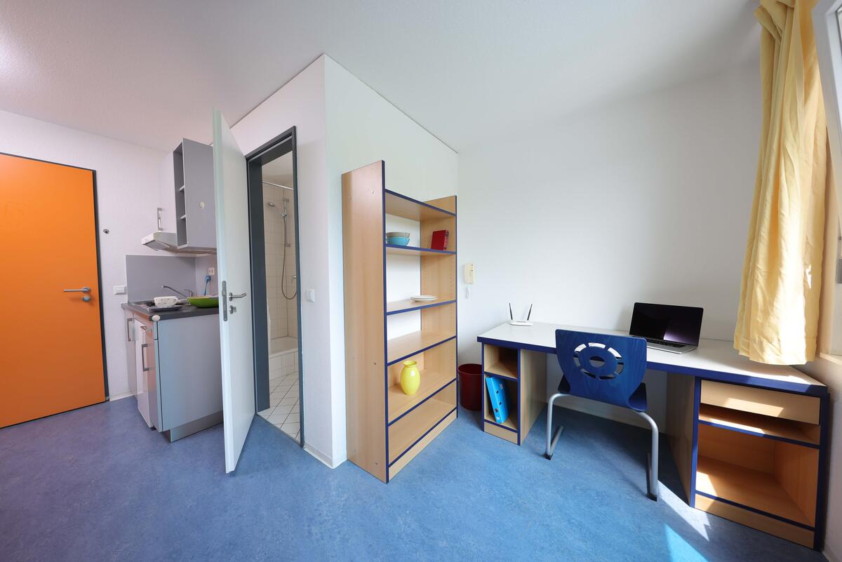 Zimmer mit Ragal, Schreibtisch und kleiner Küchenzeile in der Wohnanlage im Goerdelerweg