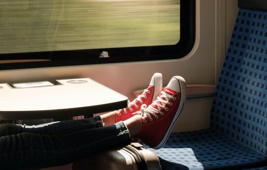 A person is riding on a train with their feet on the seat