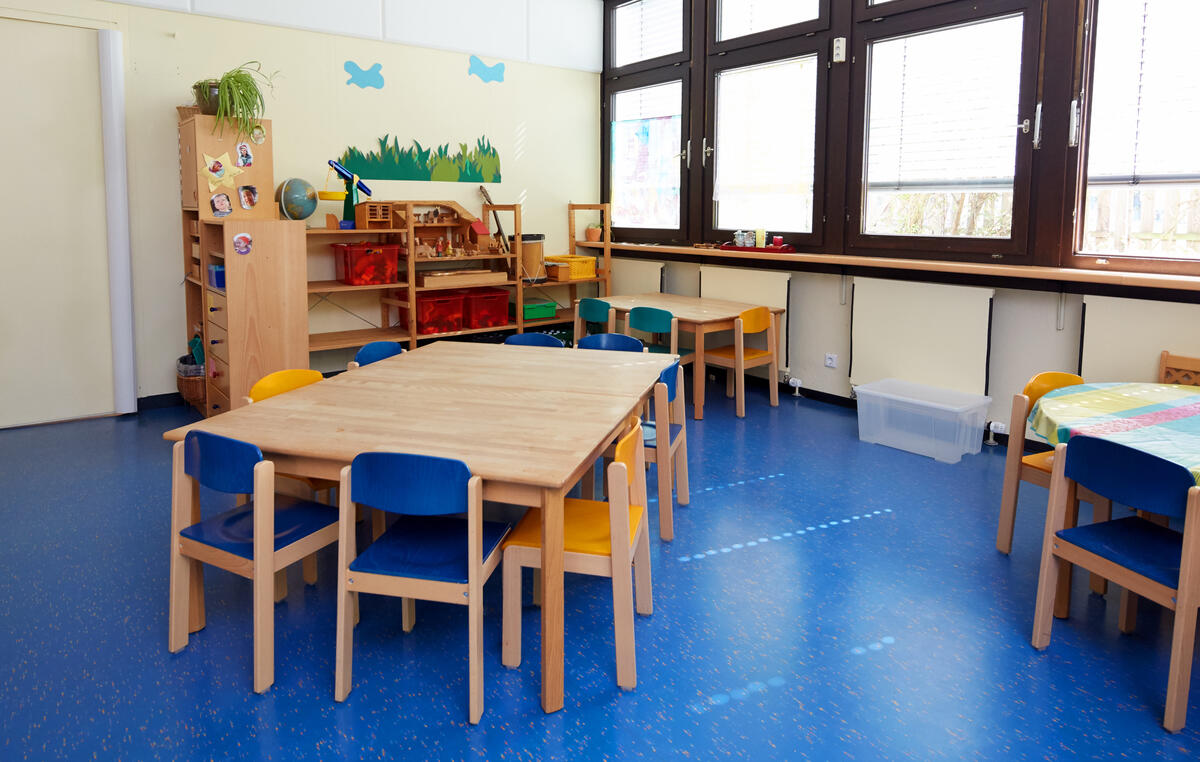 Group room with tables and chairs and large window front in the day care center Löwenzahn
