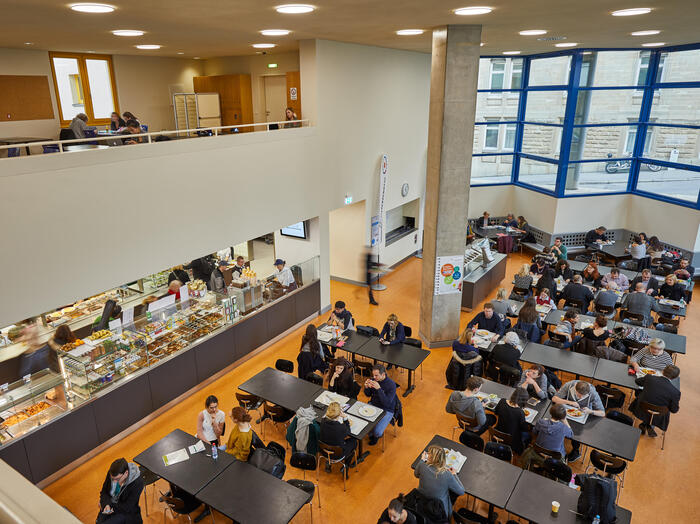 Blick von oben auf den Essensbereich mit Tischen, Stühlen und der Theke der Mensa Musikhochschule