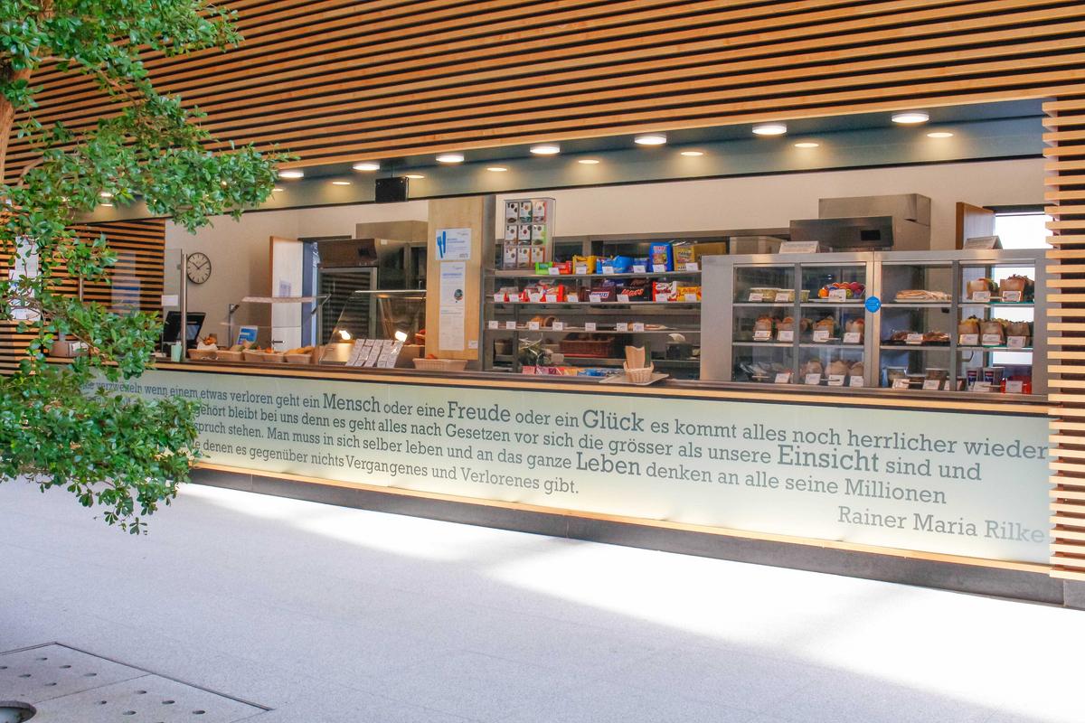 Theke der Cafeteria Göppingen mit süßen und salzigen Snacks in der Auslage. Links im Bild steht eine Pflanze