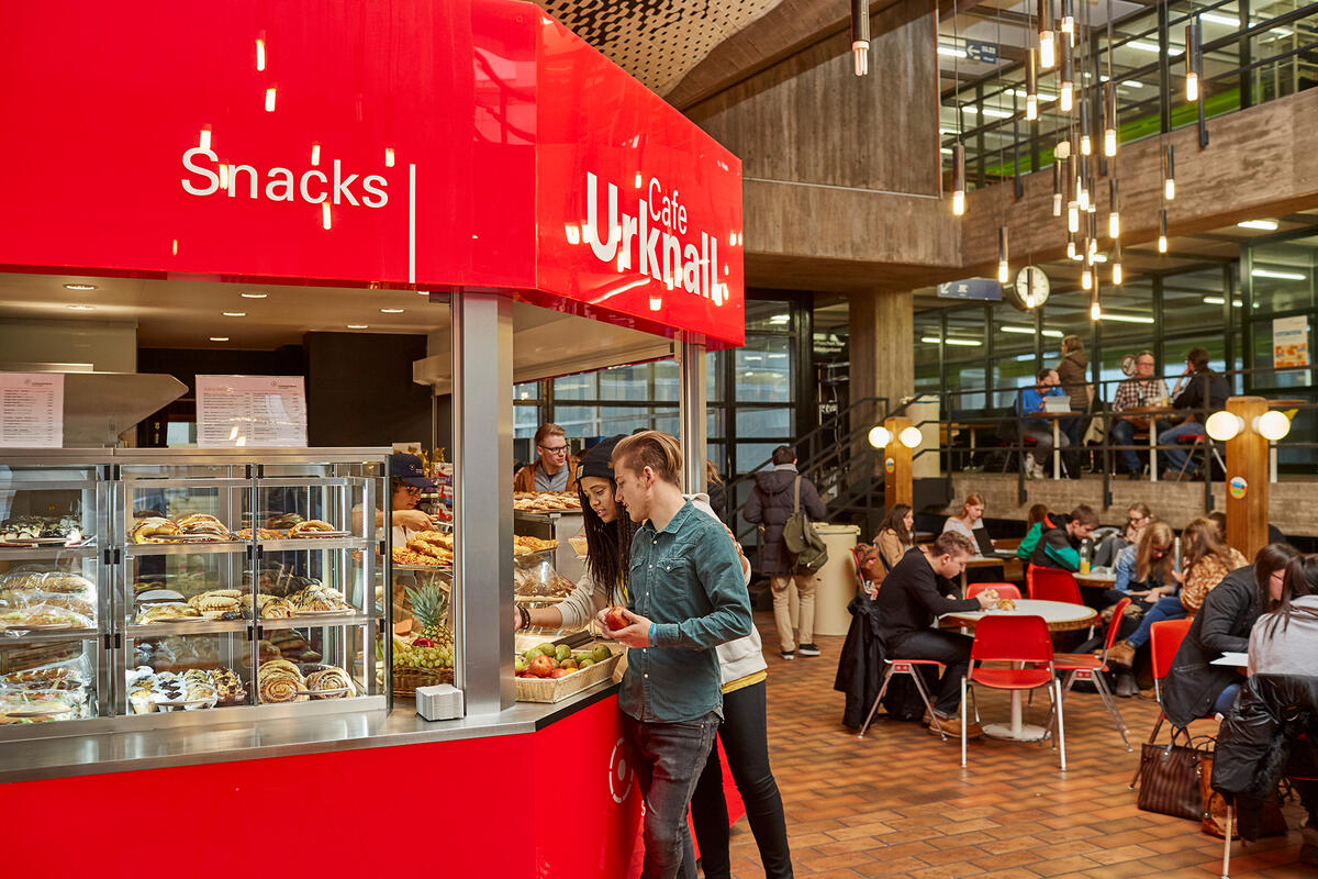 Studierende stehen an der Theke der Cafeteria Urknall und suchen sich Obst aus