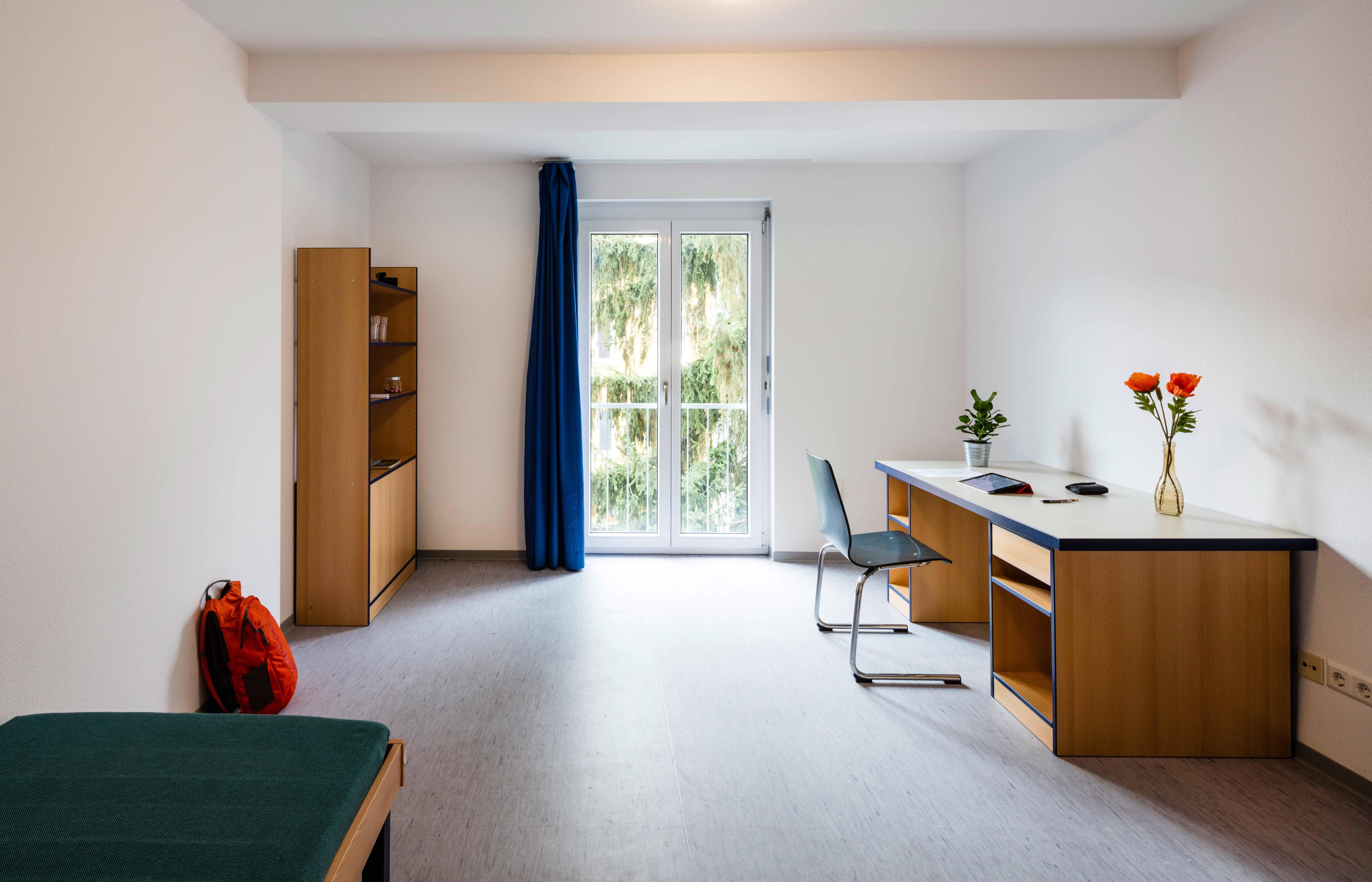 Zimmer mit Bett, Schreibtisch, Regal und großem Fenster im Studentendorf Göppingen