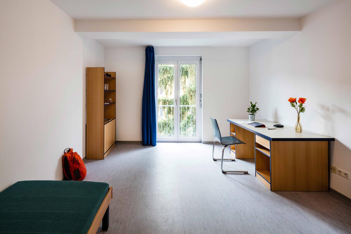 Zimmer mit Bett, Schreibtisch, Regal und großem Fenster im Studentendorf Göppingen