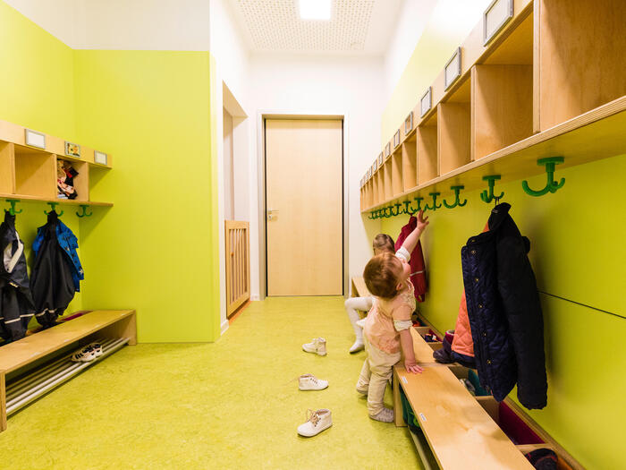 Garderobe der Villa MiO mit grünen Wänden und grünem Boden. Ein kleines Mädchen erkundet die Garderobe