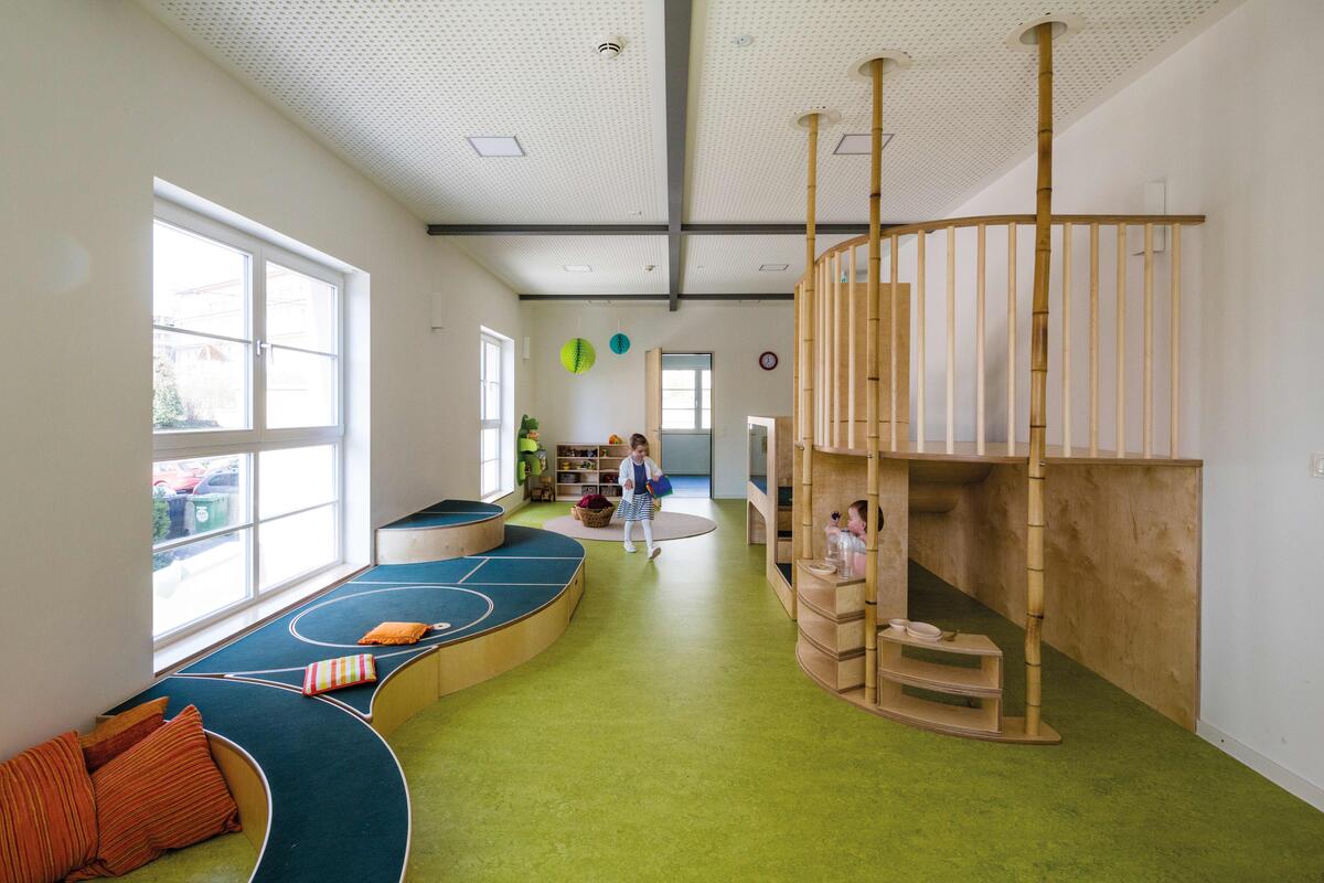 Group room of the Villa MiO day care centre with green floor and wooden platform in which two toddlers play
