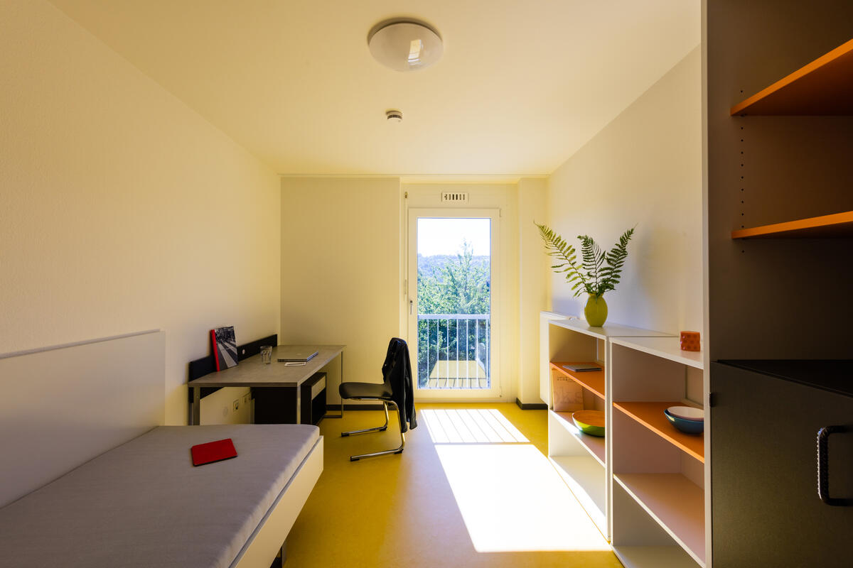 Zimmer mit Bett, Schreibtisch, Regal und großem Fenster in der Wohnanlage im Rossneckar 2