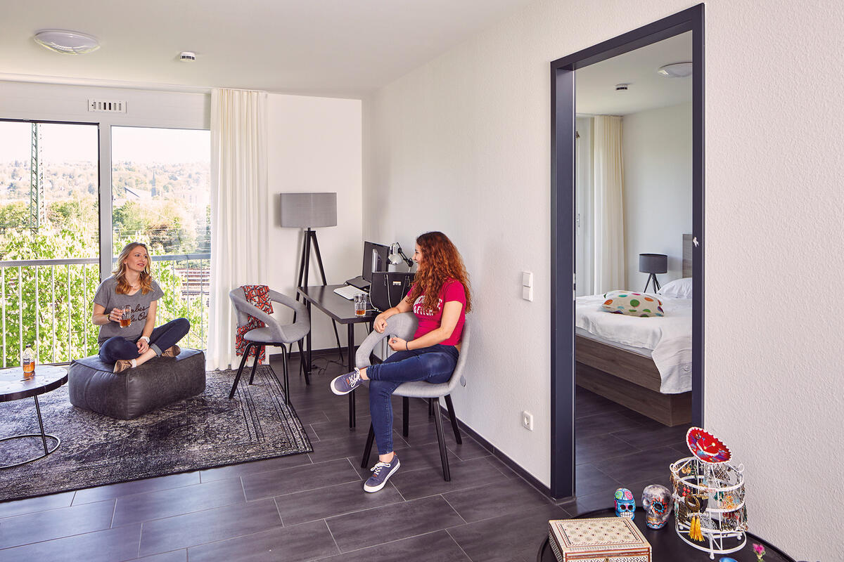 Zwei Studentinnen in einem Apartment im Boardinghaus Esslingen sitzen lachend zusammen und trinken etwas