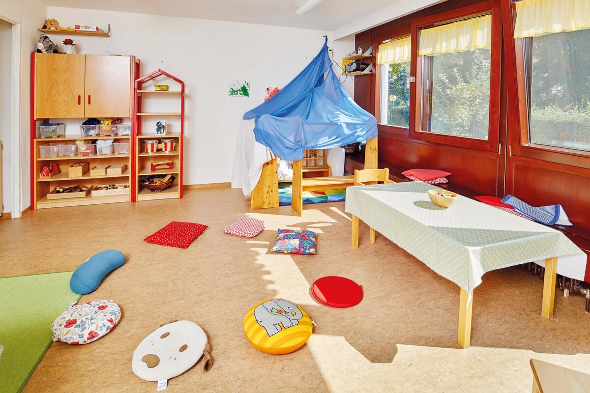 Group room with table, play corner and pillows of the Kita Hochschulezwerge