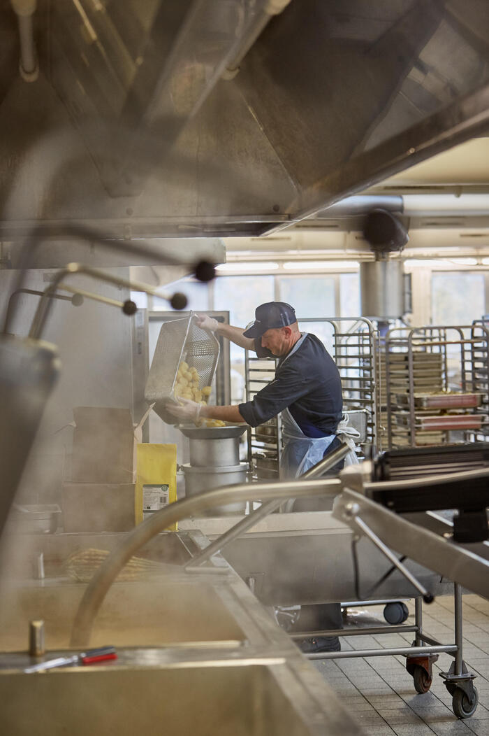 Ein Küchen-Mitarbeiter der Mensa Vaihingen, kippt Kartoffeln in die Kartoffelmaschine.