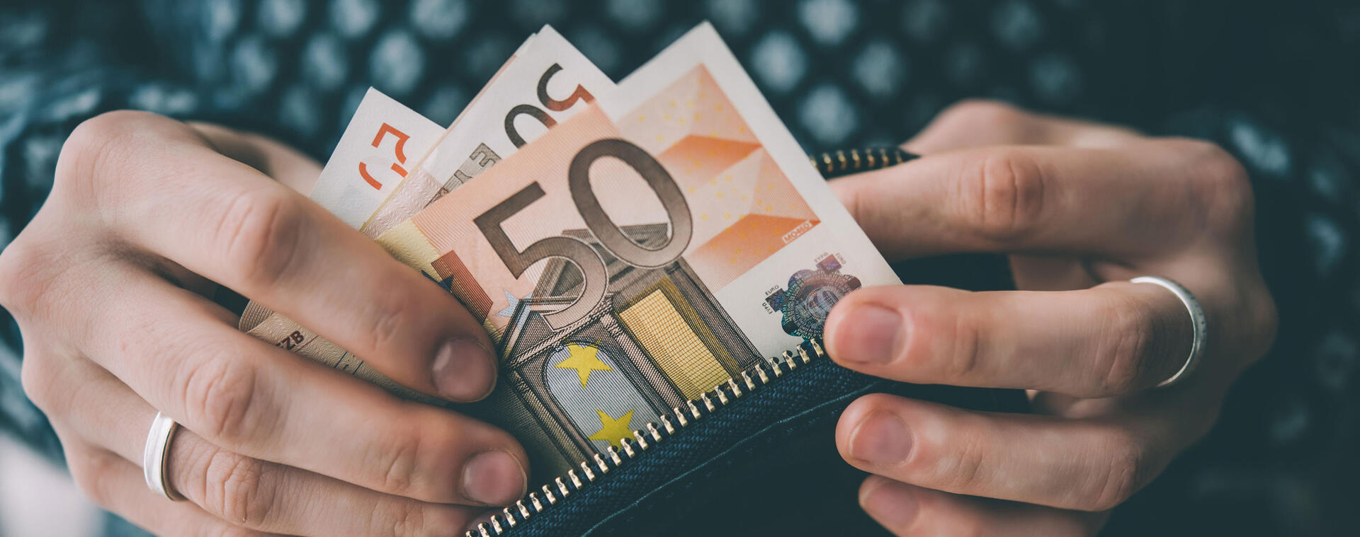 Hände halten einen Geldbeutel, aus welchem 50 Euro-Scheine genommen werden