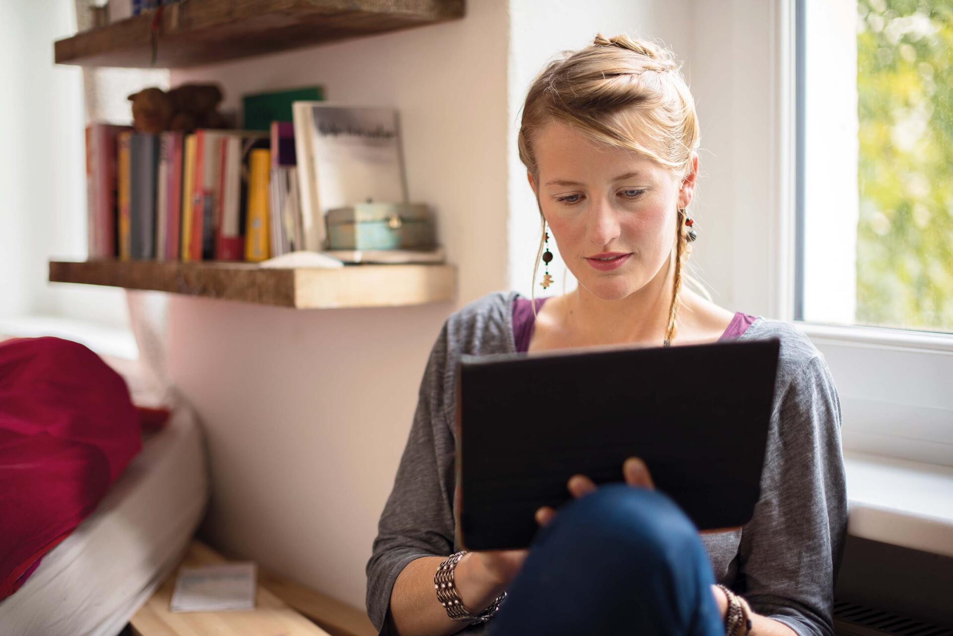 Female student sitting on a couch and holding a tablet