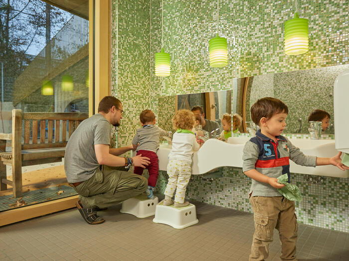 Ein Erzieher hilft drei Kindern beim Händewaschen im Badezimmer der Kita Abenteuerbande