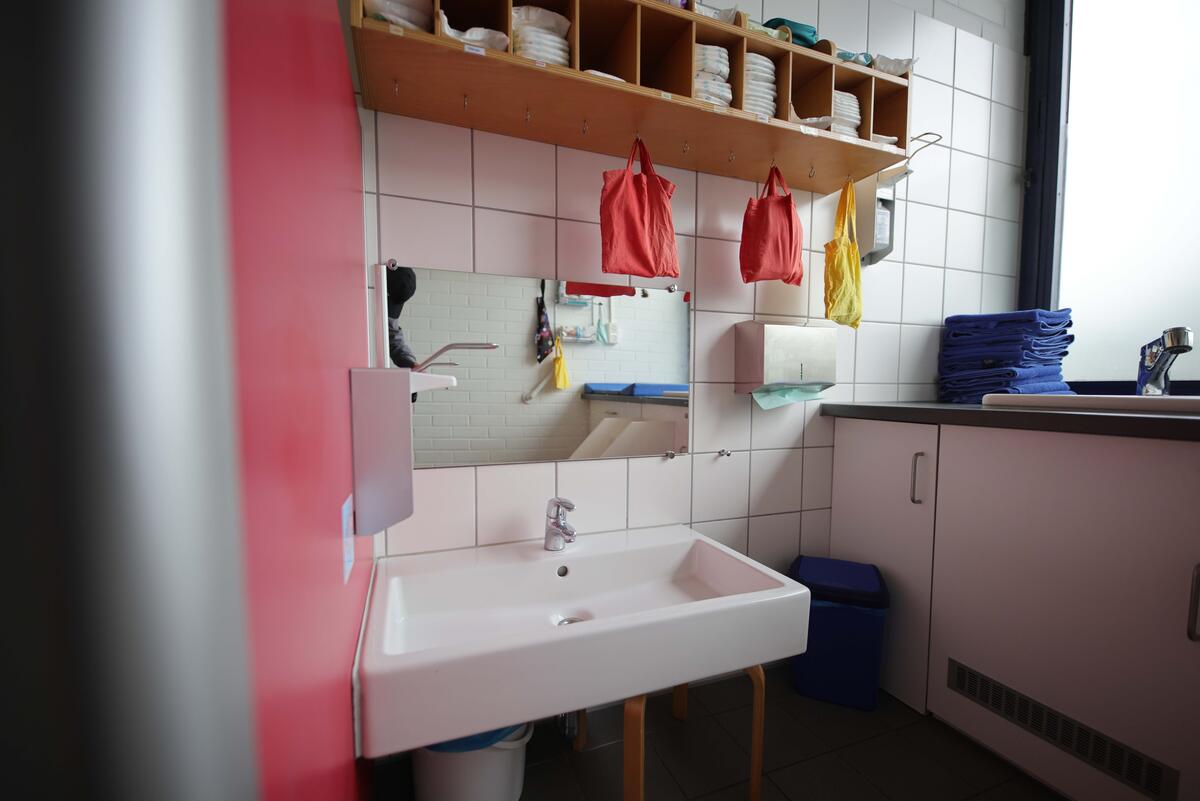 Foto vom Badezimmer in der Kita Krabbelmäuse. Es ist ein Waschbecken zu sehen, Windeln, bunte Taschen und blaue Handtücher