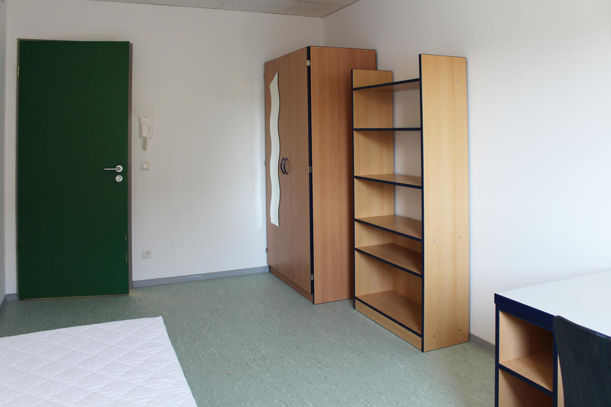 Zimmer in der Heilmannstraße mit Bett, Schrank und Regal