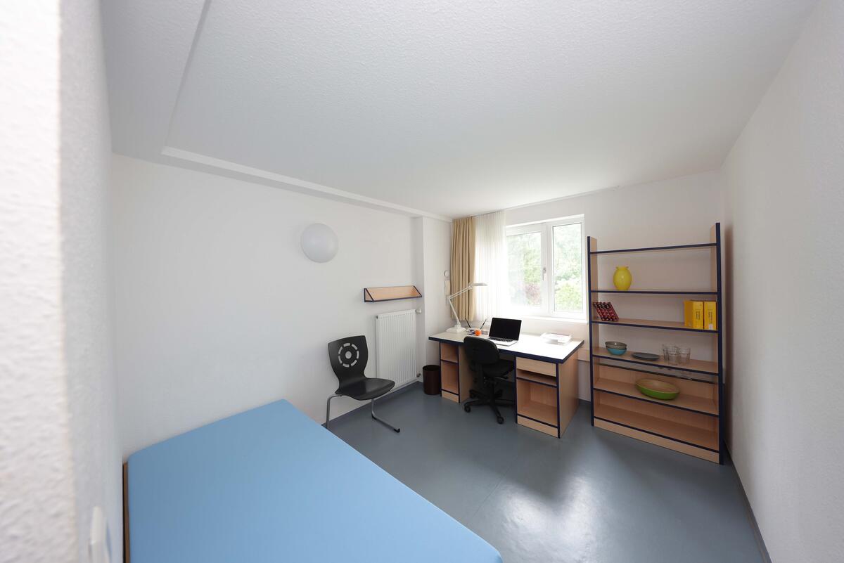 Zimmer mit Bett, Schreibtisch und Regal im Wohnheim in der Geschwister-Scholl-Straße